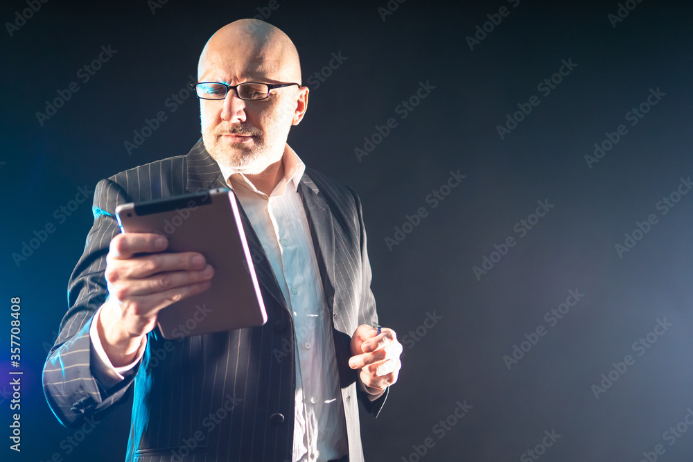 Poster human is grooving with a tablet in his hands. man on a dark background with a gadget. man with table