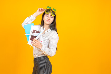 Traveler. Girl in unusual glasses for travel. A woman holds a plane ticket and documents. Model airplane in the hands of a traveler. Student was going to rest. Young woman on a yellow background