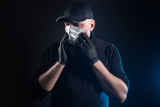 Man in a medical mask and gloves. Adult man on a dark background. Concept - human fears becoming infected. Protective measures during an epidemic. Concept - spread of infection. Gesture of despair.