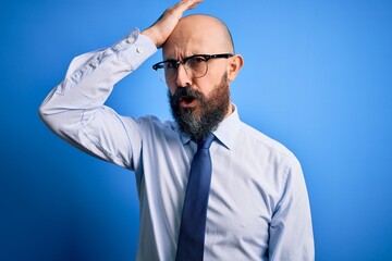 Handsome business bald man with beard wearing elegant tie and glasses over blue background...