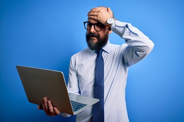 Handsome bald business man with beard working using laptop over blue background stressed with hand...