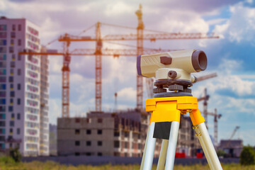 Theodolite on the background of construction cranes. Three construction cranes next to a high-rise...