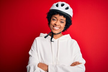 Young African American afro cyciling woman with curly hair wearing bike security helmet happy face smiling with crossed arms looking at the camera. Positive person.