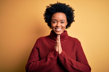 Fototapeta na wymiar Young beautiful African American afro woman with curly hair wearing casual turtleneck sweater praying with hands together asking for forgiveness smiling confident.