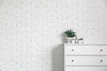 Green houseplants on chest of drawers near white brick wall
