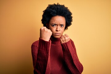 Fototapeta na wymiar Young beautiful African American afro woman with curly hair wearing casual turtleneck sweater Ready to fight with fist defense gesture, angry and upset face, afraid of problem