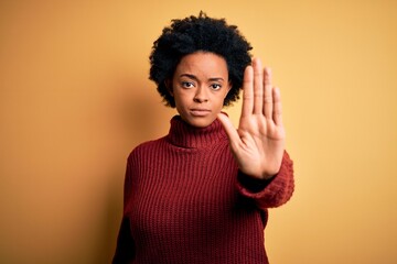 Young beautiful African American afro woman with curly hair wearing casual turtleneck sweater doing stop sing with palm of the hand. Warning expression with negative and serious gesture on the face.