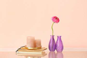 Vases with beautiful flower, notebooks and aroma candles on table near color wall
