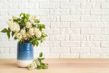 Vase with beautiful flowers on table near white brick wall