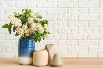 Vases with beautiful flowers on table near white brick wall