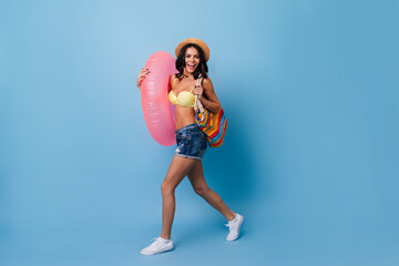 Blissful girl with swimming circle dancing on blue background. Studio shot of carefree lady in summer attire.