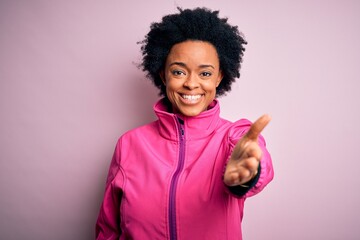 Young African American afro sportswoman with curly hair wearing sportswear doin sport smiling friendly offering handshake as greeting and welcoming. Successful business.