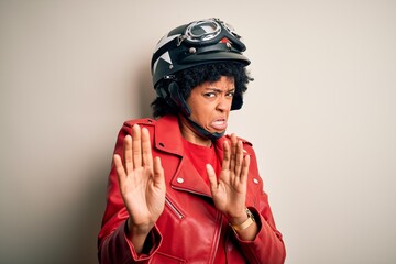 Young African American afro motorcyclist woman with curly hair wearing motorcycle helmet disgusted expression, displeased and fearful doing disgust face because aversion reaction. With hands raised