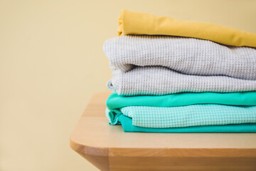 Stack of clean clothes on stool against color background, closeup