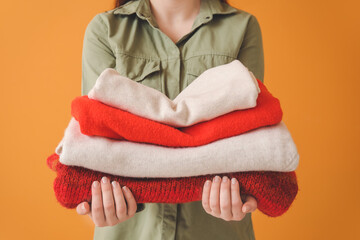 Woman with stack of clean clothes on color background, closeup