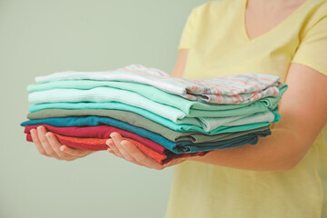 Woman with stack of clean clothes on color background, closeup