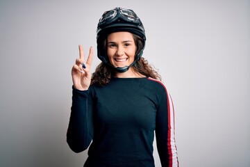 Beautiful motorcyclist woman with curly hair wearing moto helmet over white background smiling with happy face winking at the camera doing victory sign. Number two.
