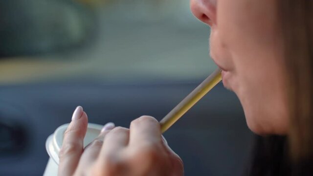 Woman drinks a drink from a paper cup through a straw in a car. Slow motion