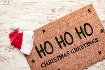 Door mat with Christmas greeting and Santa hat on wooden background