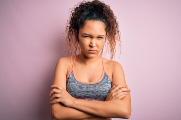 Beautiful sportswoman with curly hair doing sport wearing sportswear over pink background skeptic...