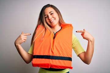Young beautiful blonde woman with blue eyes wearing orange lifejacket over white background looking...
