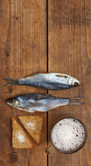 Two salted fish, toast with salt and a beer mug on a wooden background on top with space