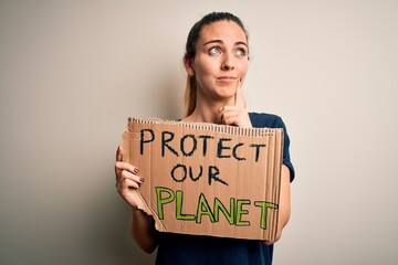 Young beautiful blonde woman with blue eyes asking for protect planet holding banner serious face thinking about question, very confused idea