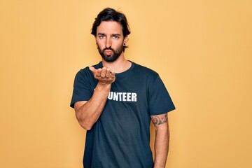 Young handsome hispanic volunteer man wearing volunteering t-shirt as social care looking at the...
