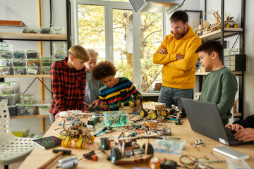 Our challenge is our progress. Young technicians building a robot vehicle together with a male...