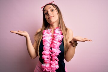 Young beautiful blonde woman wearing swimsuit and floral Hawaiian lei over pink background clueless...