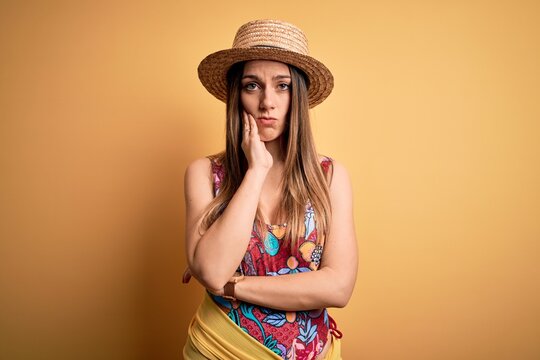 Young beautiful blonde woman wearing swimsuit and summer hat over yellow background thinking looking tired and bored with depression problems with crossed arms.