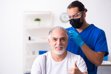 Obraz premium Old man visiting young male doctor in hair transplantation conce