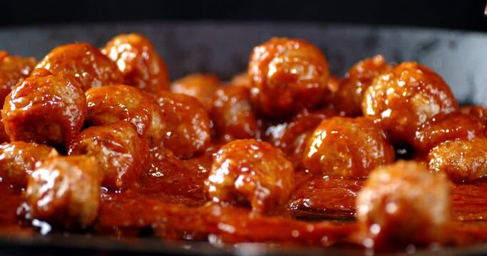 Ready meatballs in tomato sauce stirred with a wooden spatula.