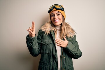 Young brunette skier woman wearing snow clothes and ski goggles over white background smiling swearing with hand on chest and fingers up, making a loyalty promise oath