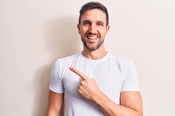 Young handsome man wearing casual t-shirt standing over isolated white background smiling cheerful pointing with hand and finger up to the side