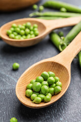 Spoons with tasty fresh peas on dark background