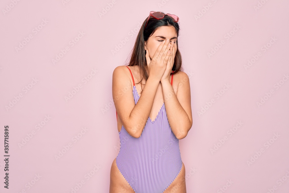 Sticker Young beautiful fashion girl wearing swimwear swimsuit and sunglasses over pink background with sad expression covering face with hands while crying. Depression concept.