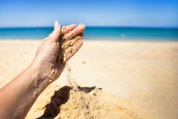 Fototapeta na wymiar A stream of sand falls from the hand of a woman on a sandy beach