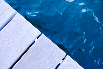 Wooden dock and water in cool evening light, edges of teak planks and blurred dark blue water with reflections.