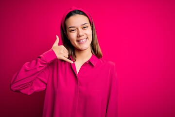 Young beautiful brunette girl wearing casual shirt standing over isolated pink background smiling doing phone gesture with hand and fingers like talking on the telephone. Communicating concepts.