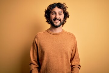 Young handsome man with beard wearing casual sweater standing over yellow background with a happy and cool smile on face. Lucky person.
