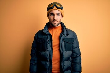 Young handsome skier man with beard wearing snow sportswear and ski goggles Relaxed with serious expression on face. Simple and natural looking at the camera.