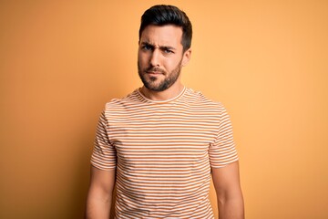 Young handsome man with beard wearing casual striped t-shirt over yellow background skeptic and nervous, frowning upset because of problem. Negative person.