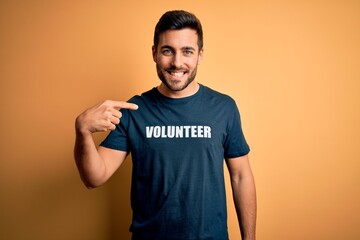 Young handsome man with beard volunteering wearing t-shirt with volunteer message with surprise face pointing finger to himself