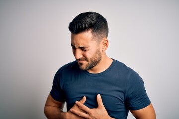 Young handsome man wearing casual t-shirt standing over isolated white background with hand on stomach because indigestion, painful illness feeling unwell. Ache concept.