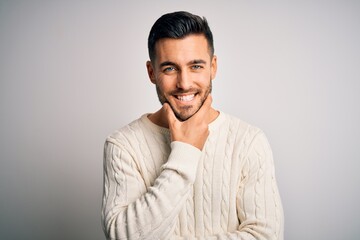 Obraz premium Young handsome man wearing casual sweater standing over isolated white background looking confident at the camera smiling with crossed arms and hand raised on chin. Thinking positive.