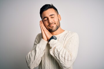 Young handsome man wearing casual sweater standing over isolated white background sleeping tired dreaming and posing with hands together while smiling with closed eyes.