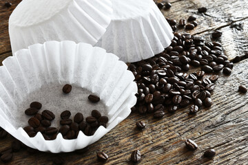 An image of several white basket style coffee filers and dark roasted coffee beans. 
