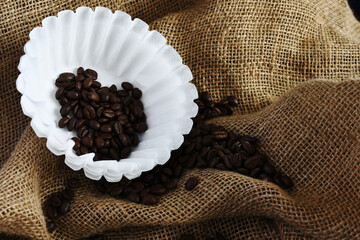 An image of several white basket style coffee filers and dark roasted coffee beans. 