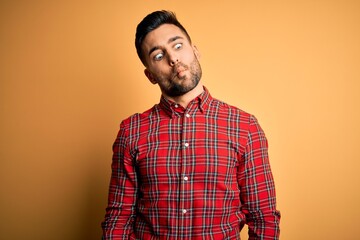 Fototapeta premium Young handsome man wearing casual shirt standing over isolated yellow background making fish face with lips, crazy and comical gesture. Funny expression.